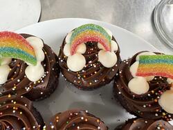 chocolate cupcakes with chocolate frosting, rainbow sprinkles, and sour rainbow rope to look like rainbows