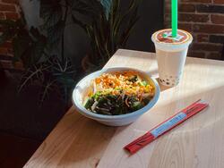 boba tea, a bowl of ramen, and chopsticks in the sun on a table